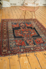 Tattered ends and intricate red, blue, ivory geometric border of the antique Kamseh rug.