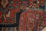 Corner of antique Kamseh rug, showing madder red pile, navy blue designs, and restrung tattered fringe.
