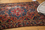 Vintage Baktiari rug corner with distressed red rust and navy patterns, exposed foundation.