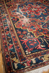 Distressed vintage Baktiari rug pile, geometric patterns in red, navy, and saffron, with fringe.