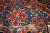 Distressed Baktiari rug, hand-knotted pile featuring red, navy geometric motifs, and fringe.