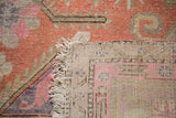 Antique Khotan rug corner, showing distressed terra cotta and pink pile, white fringe, and hand-knotted back.