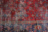 Splayed floral design elements on distressed cherry red and navy blue vintage Mahal carpet.