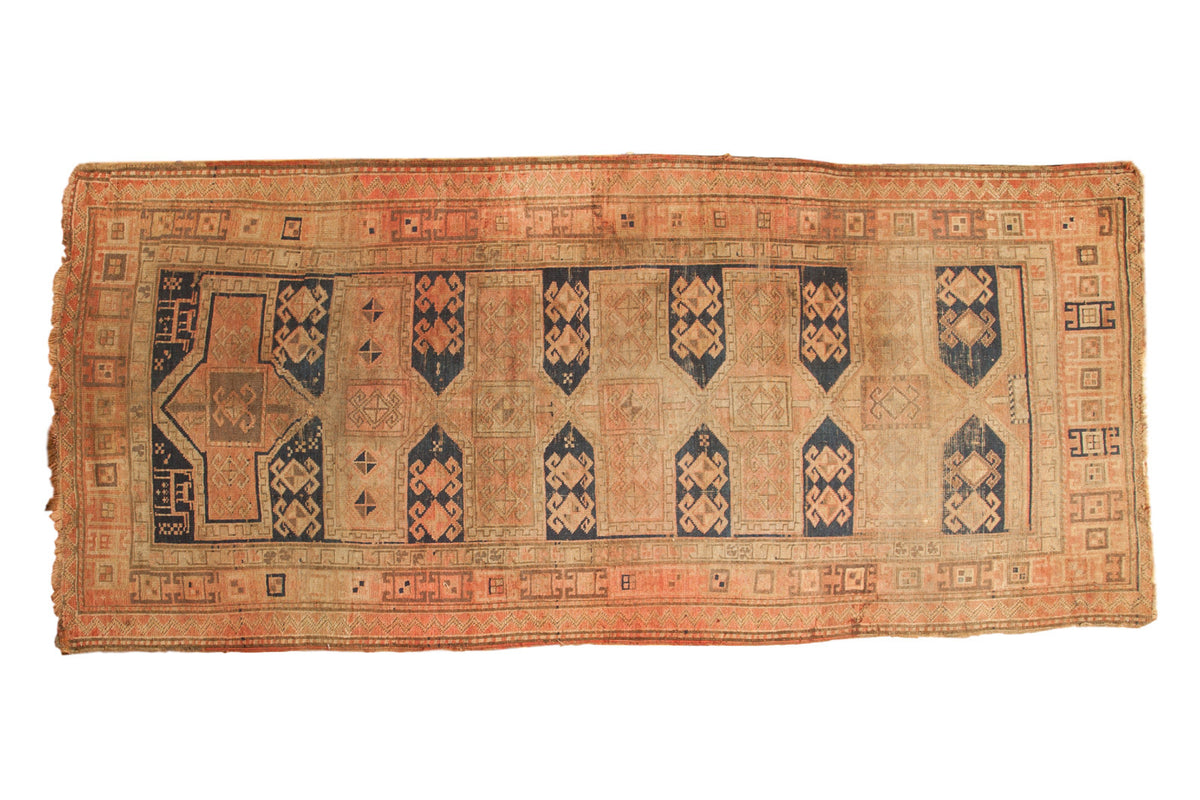 Antique Caucasian runner rug with navy geometric medallions, crab motifs, sand field, blush border.