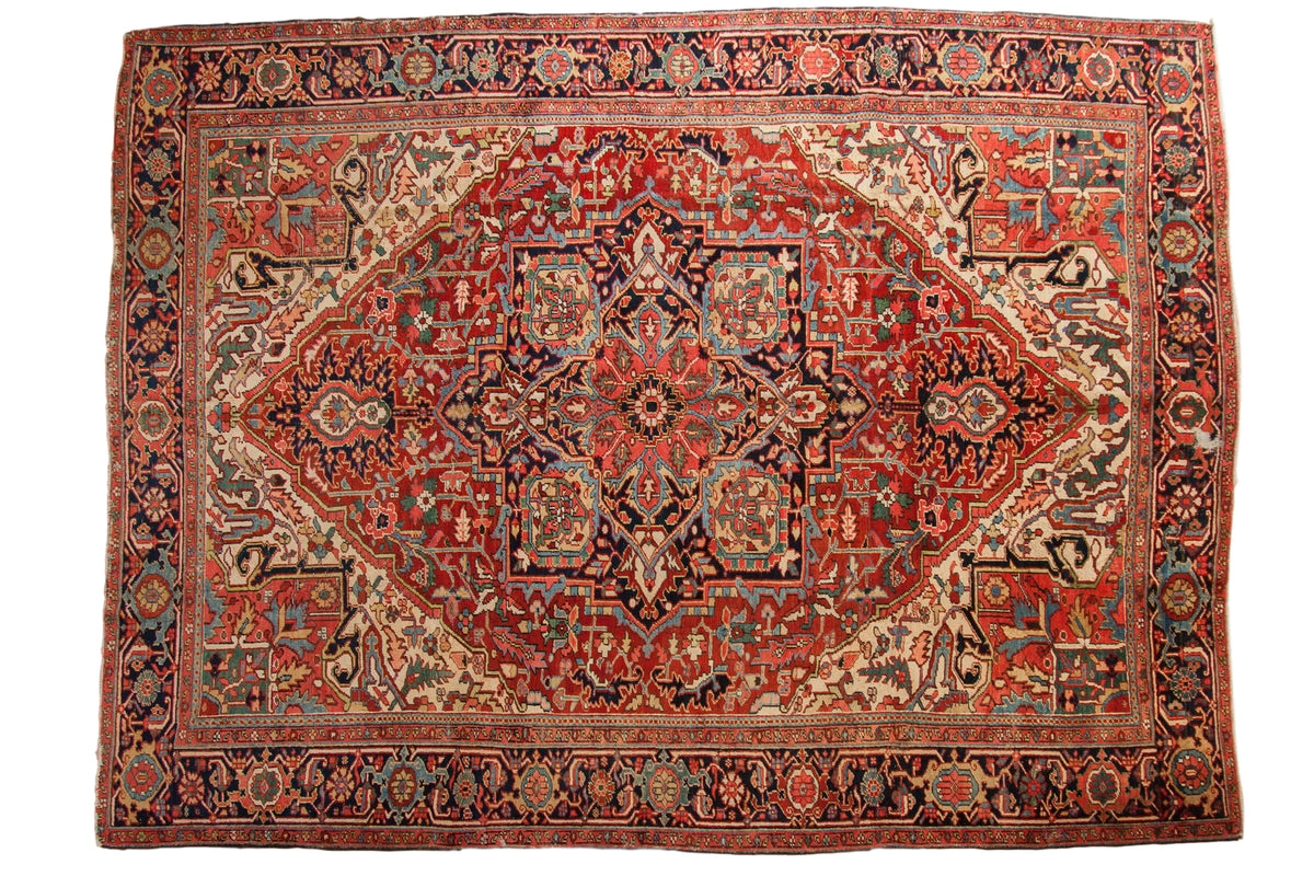 Vintage Heriz carpet with ruby red field, navy blue borders, central medallion, and arabesque spandrels.