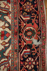 Vintage Heriz rug with gem-toned red, navy, cream patterns, areas of foundation showing.