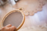 Vintage natural wood embroidery hoop held by hand with taut light grey fabric.
