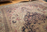 Unrolling an antique Persian Kermanshah carpet, showing its dense navy medallion and ivory floral field.