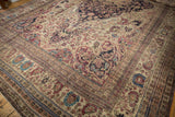 Angled view of an antique Kermanshah carpet's intricate floral corner and navy medallion.
