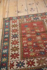 Antique Kazak rug's geometric starburst border, abstract field motifs, madder red, blue.