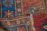 Vintage Caucasian carpet folded corner with worn terra cotta, indigo gul motif pile, and fringe.