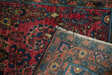 Folded vintage German Sarouk rug showing hand knotted foundation, woven fringe, and rich red floral motifs.