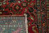 Vintage Persian Sarouk rug corner with cherry red floral pile, knotted foundation, and white fringe.