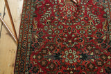 Vintage Sarouk runner's cherry red pile with intricate floral bouquets and detailed patterned border.