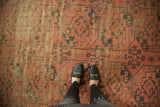 Antique Ensi carpet: repeating dark blush, navy charcoal gul motifs, visible wear, and feet.