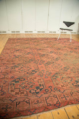 Repeating oversized gul motifs across an antique Afghan Ensi rug, brick red and navy.