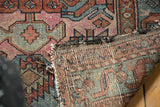 Tattered side and exposed foundation of vintage Mehriban rug with dusty magenta and teal pattern.