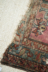 Corner detail of the vintage Mehriban rug, with tattered fringe, worn magenta and teal field.