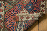 Folded corner of antique Jaff Kurd rug, showing geometric madder red, indigo blue motifs and fringe.