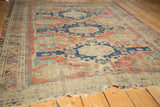 Aged Caucasian Soumac rug with an elongated navy medallion, red floral field, and tattered border.