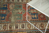 Geometric madder red, blue, and ivory patterns, plus visible tatter on an antique Caucasian rug.