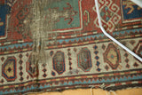 Textured close-up of the antique Caucasian rug's tattered edge and threadbare geometric border.