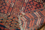 Detail of antique Turkmen rug: tattered fringe, perimeter hole, red and navy geometric motifs.