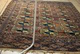 Angled view of hand-knotted vintage Turkmen rug with triple Bokhara gul motifs in eggplant and apricot.