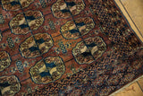 Russet field with antique ivory and navy Bokhara guls, geometric border, and fringe.