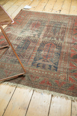 Antique Belouch rug corner: faded pomegranate, indigo geometric, visible restrung foundation, light fringe.