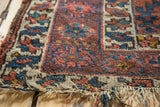 Worn vintage Caucasian rug runner showing exposed foundation and tattered fringe.
