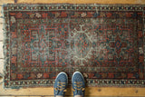 Geometric Karaja rug corner: cherry red, mallard green pattern, with beige tones and tattered fringe.