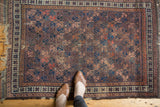 Antique Belouch rug with geometric lattice pattern, aubergine, mauve, terra cotta, and frayed edges.