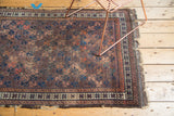 Antique Belouch rug corner, revealing tattered edge and geometric field pattern.