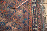 Antique Belouch rug's tattered edge, geometric border patterns, and aubergine lattice field.