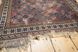 Antique Belouch rug border with geometric motifs, rich aubergine hues, and tattered fringe.