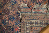 Folded antique Belouch rug showing aubergine, terracotta pile, geometric back, tattered fringe.