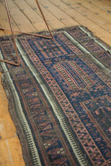 Antique Persian Belouch rug detail: indigo field, aubergine Laleh Abbasi pattern, ivory stripe, and tattered edge.