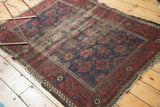 Antique Belouch rug corner, revealing tattered edges, worn foundation, and faded indigo floral field.
