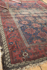 Antique Persian Belouch rug corner with tattered fringe, indigo, red and figural border motifs.