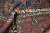 Antique Belouch rug folded, showing hand-knotted foundation, worn fringe, and indigo, wine red pile.