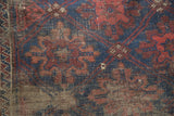 Antique Belouch rug's worn indigo, wine red pile, exposed foundation, and small interior hole.
