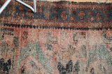 Vintage Persian Lilihan rug close-up: worn dusty rose field, exposed foundation, and teal border.