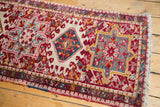 Karaja runner close-up of mallard green diamond medallion on ivory and cherry red geometric field, with colorful selvage.