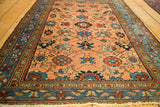 Angled view of an antique Persian Lilihan rug's floral peach field, blue border, and fringe.