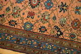 Intricate floral vinery on a peach apricot field and patterned blue border of an antique Lilihan rug.