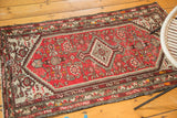 Vintage Hamadan rug's lower corner, featuring aged cinnabar red and ivory geometric patterns.