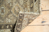 Vintage Caucasian rug corner displaying geometric stepped patterns, floral cross-sections, and lightly tattered fringe.