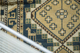 Geometric diamond panel and animal figure on a vintage Caucasian rug in dusty teal.