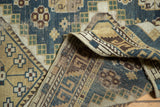 Detail of vintage Caucasian rug's geometric patterns and machine-bound side in dusty teal and beige.